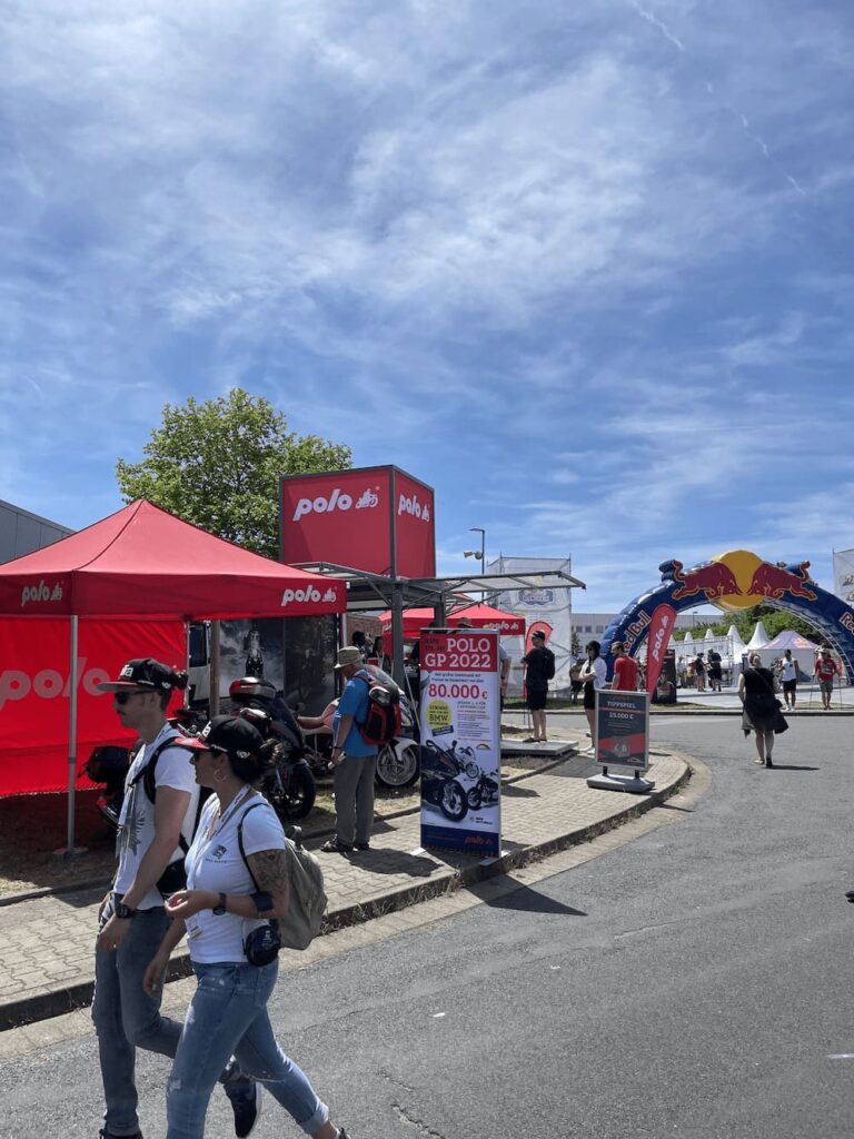 Bild von Menschen auf einer Straße auf welcher ein roter Stand von POLO zu sehen ist.